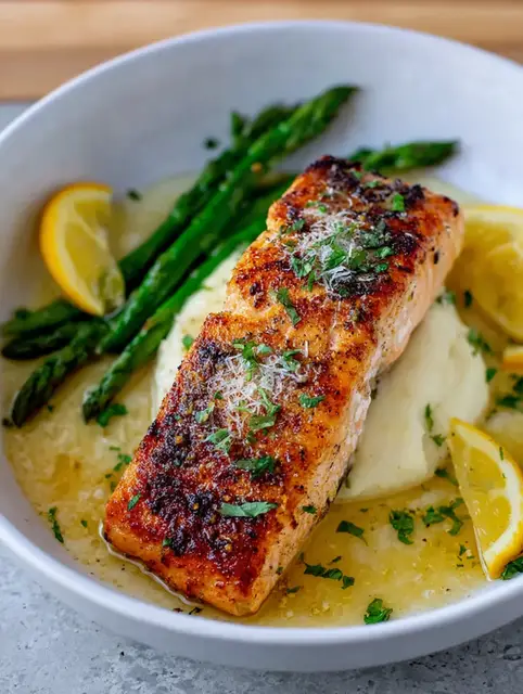 Plated baked lemon garlic butter salmon with fresh parsley, lemon slices, mashed potatoes, and steamed greens.