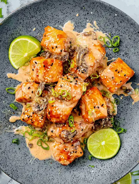 Crispy Bang Bang Salmon bites served with lime wedges and dipping sauce on a plate.