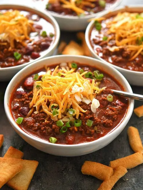 Bowl of best chili recipe topped with cheese and green onions, showcasing fresh ingredients like beans and tomatoes.