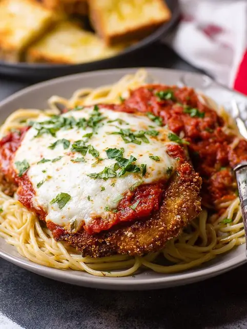 Classic Veal Parmesan plated elegantly with spaghetti, fresh basil, and grated cheese, showcasing the rich colors of the dish.