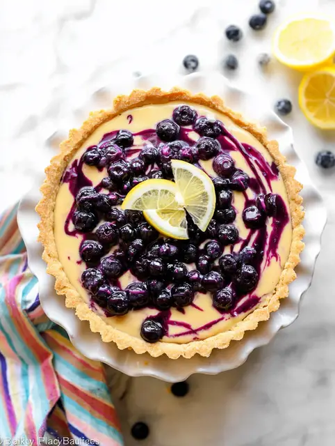 Lemon blueberry tart with fresh blueberries and lemon slices on a wooden table.