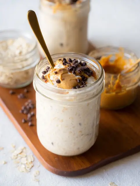Mason jar of blended overnight oats topped with fresh berries and maple syrup on a wooden table.