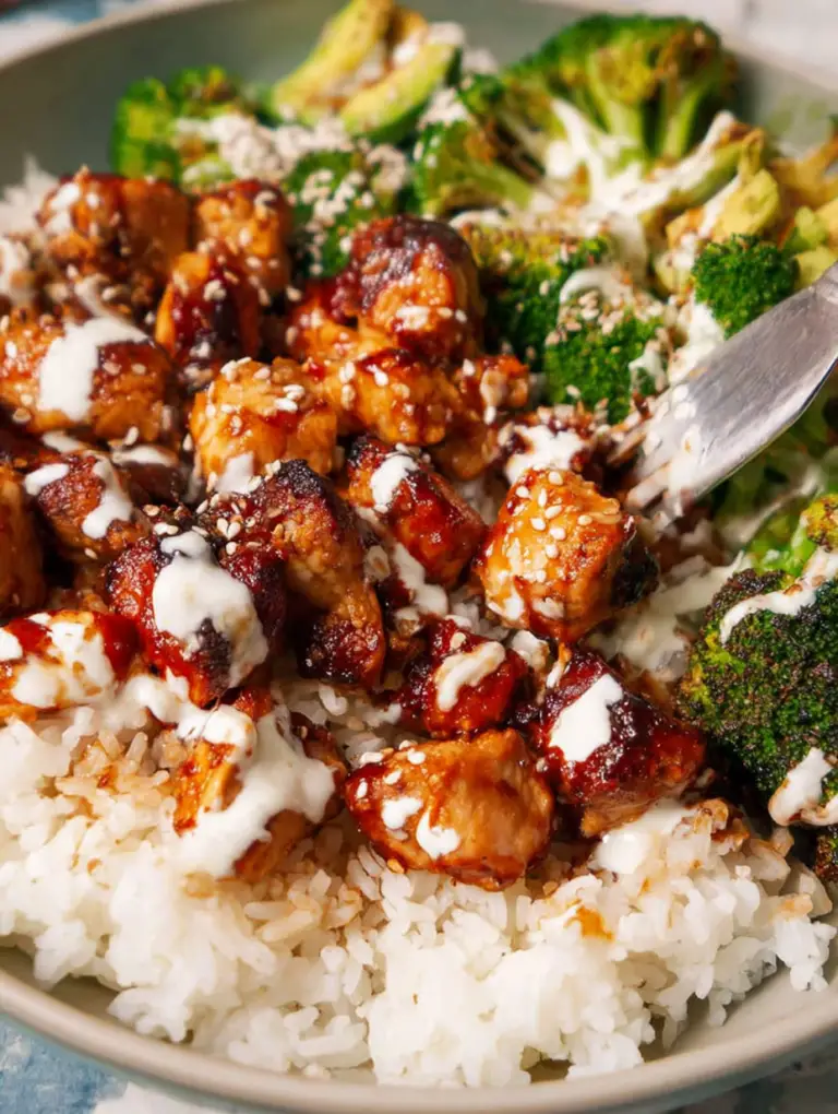 Close-up of sticky chicken bowl with chicken, rice, green onions, and sesame seeds.