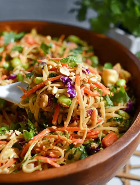 Thai Spring Roll Pasta Salad with colorful vegetables and shrimp in a bowl, garnished with peanuts and dressing.