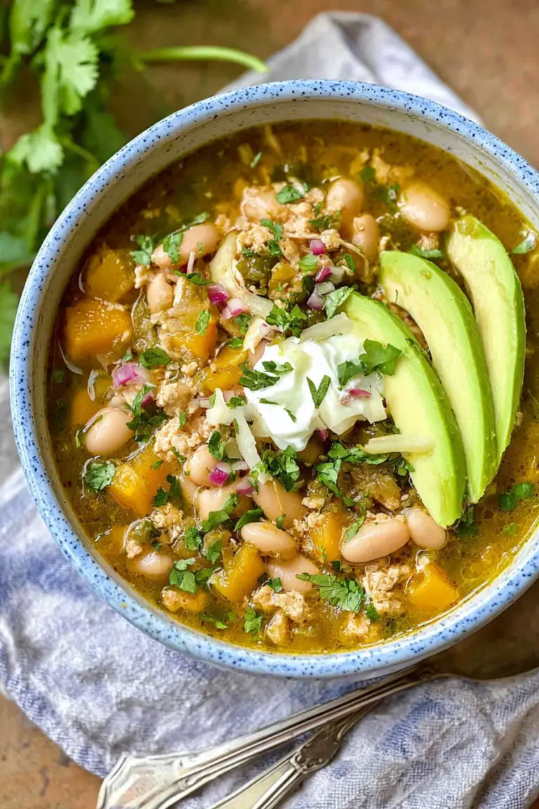 Delicious bowl of easy white bean turkey chili verde with avocado and cilantro on a wooden table.