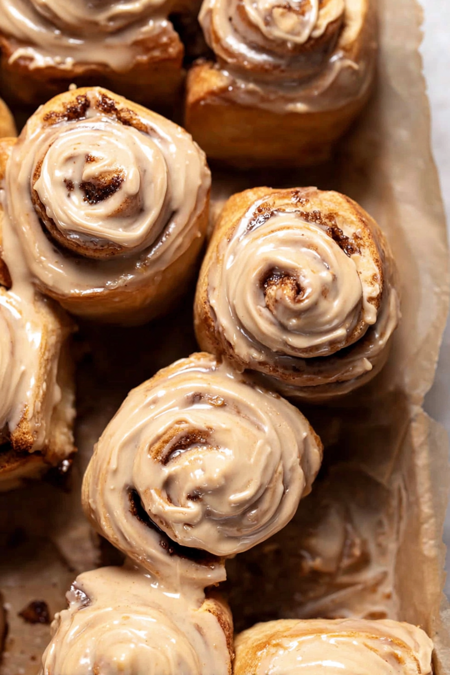 Freshly baked coffee rolls with cream cheese frosting on a tray, accompanied by a steaming cup of coffee.
