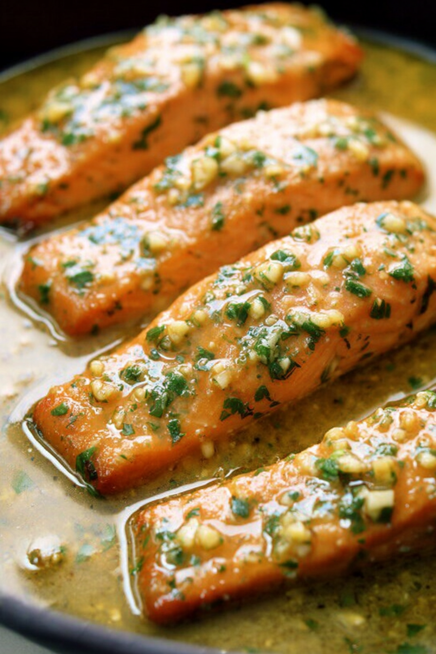 Close-up of garlic butter salmon fillets garnished with parsley and lemon wedges on a white plate.