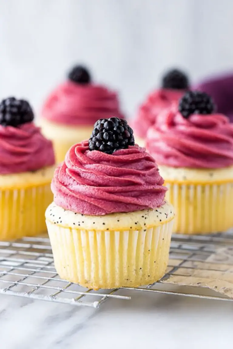Lemon poppy seed cupcake with blackberry frosting and fresh blackberries on a plate.
