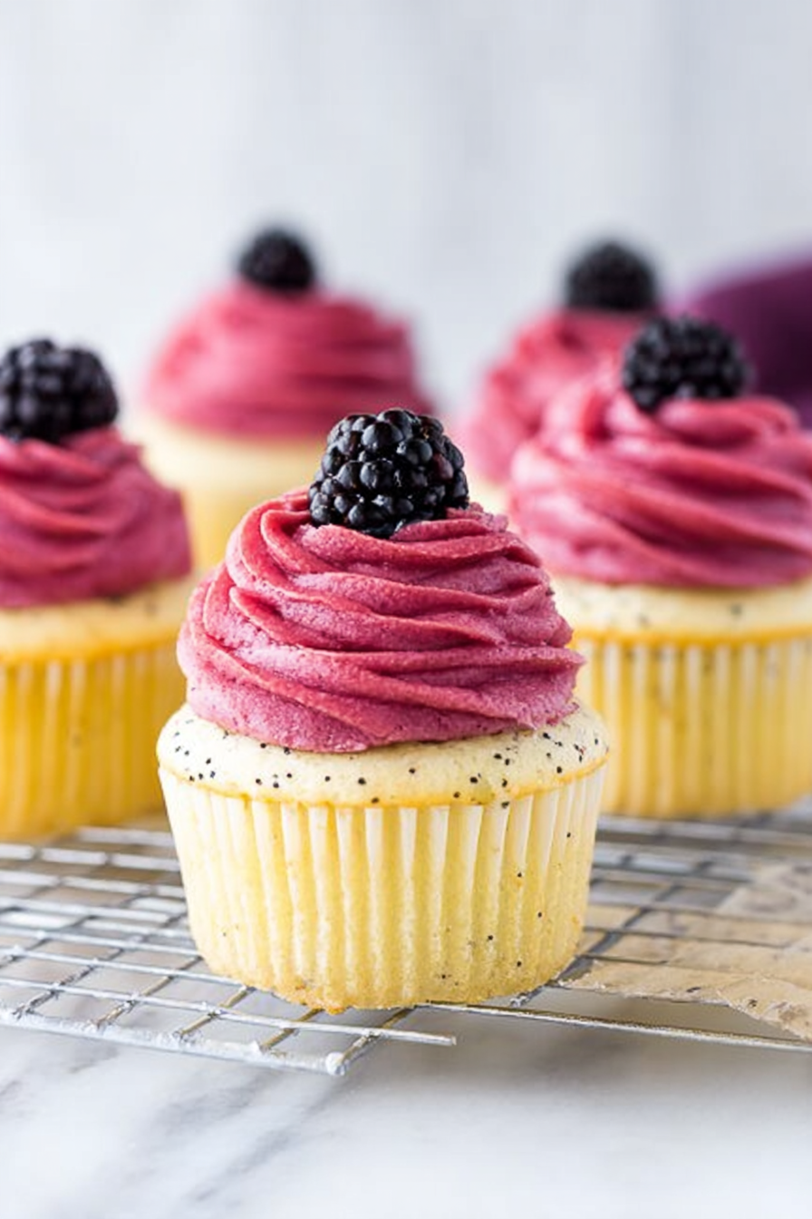 Lemon poppy seed cupcake with blackberry frosting and fresh blackberries on a plate.