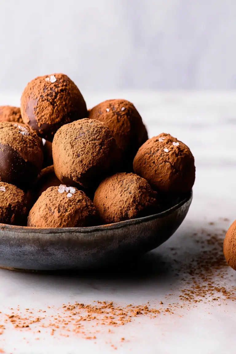 Close-up of salted caramel truffles coated in cocoa powder and topped with sea salt on a wooden table.