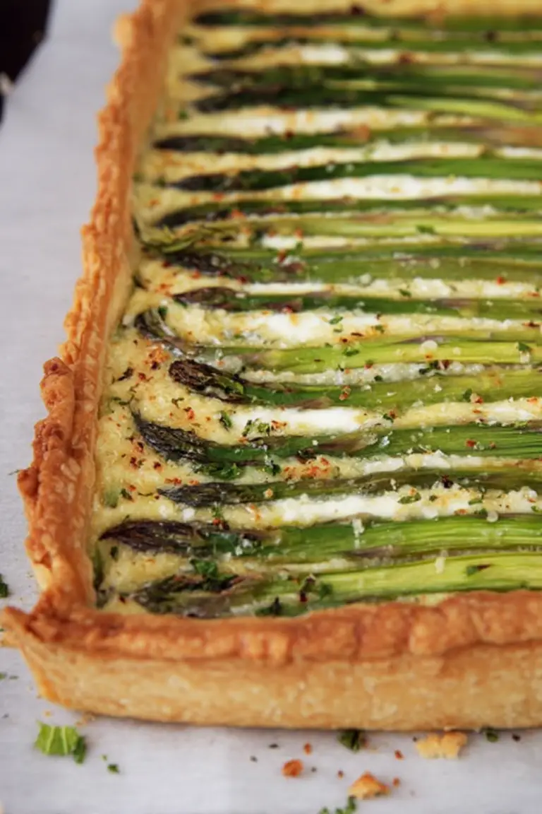 Asparagus gruyere tart served on a wooden table with fresh asparagus and ingredients showcasing its spring freshness.