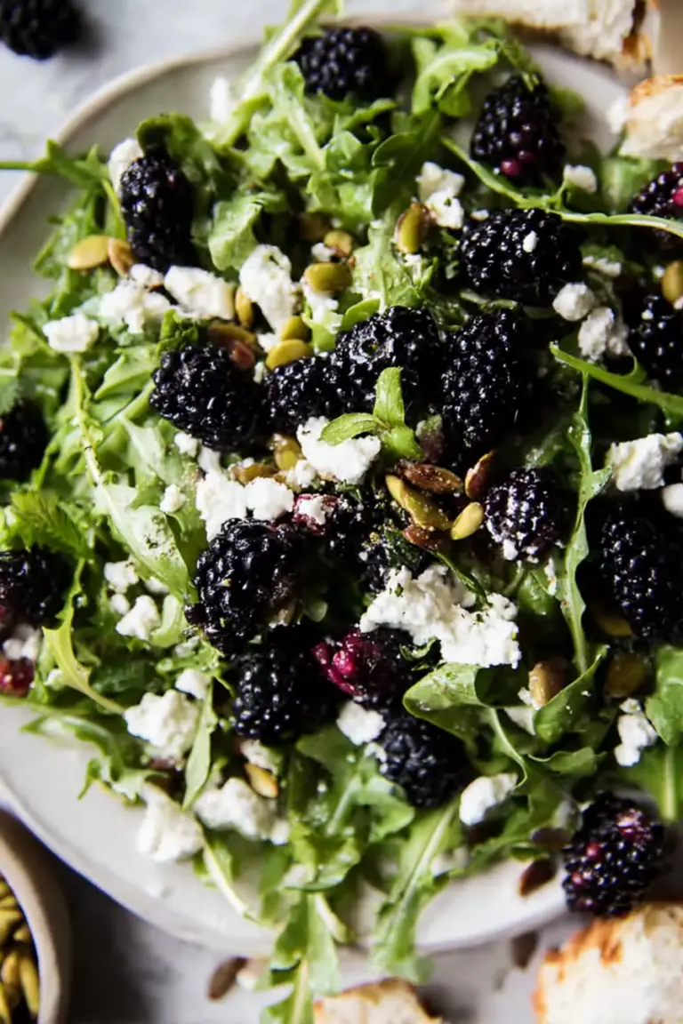 Blackberry goat cheese salad featuring arugula, ripe blackberries, goat cheese, and pistachios on a rustic bowl.