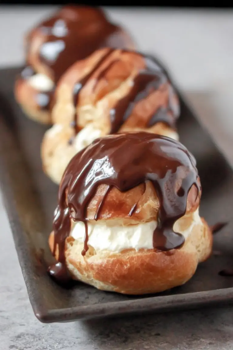 Classic French profiteroles topped with warm chocolate sauce and garnished with fresh mint, served on a white plate.