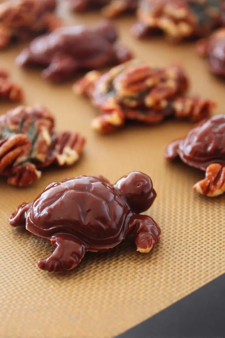 Close-up of homemade turtles candy with caramel, pecans, and chocolate drizzle on a wooden table.
