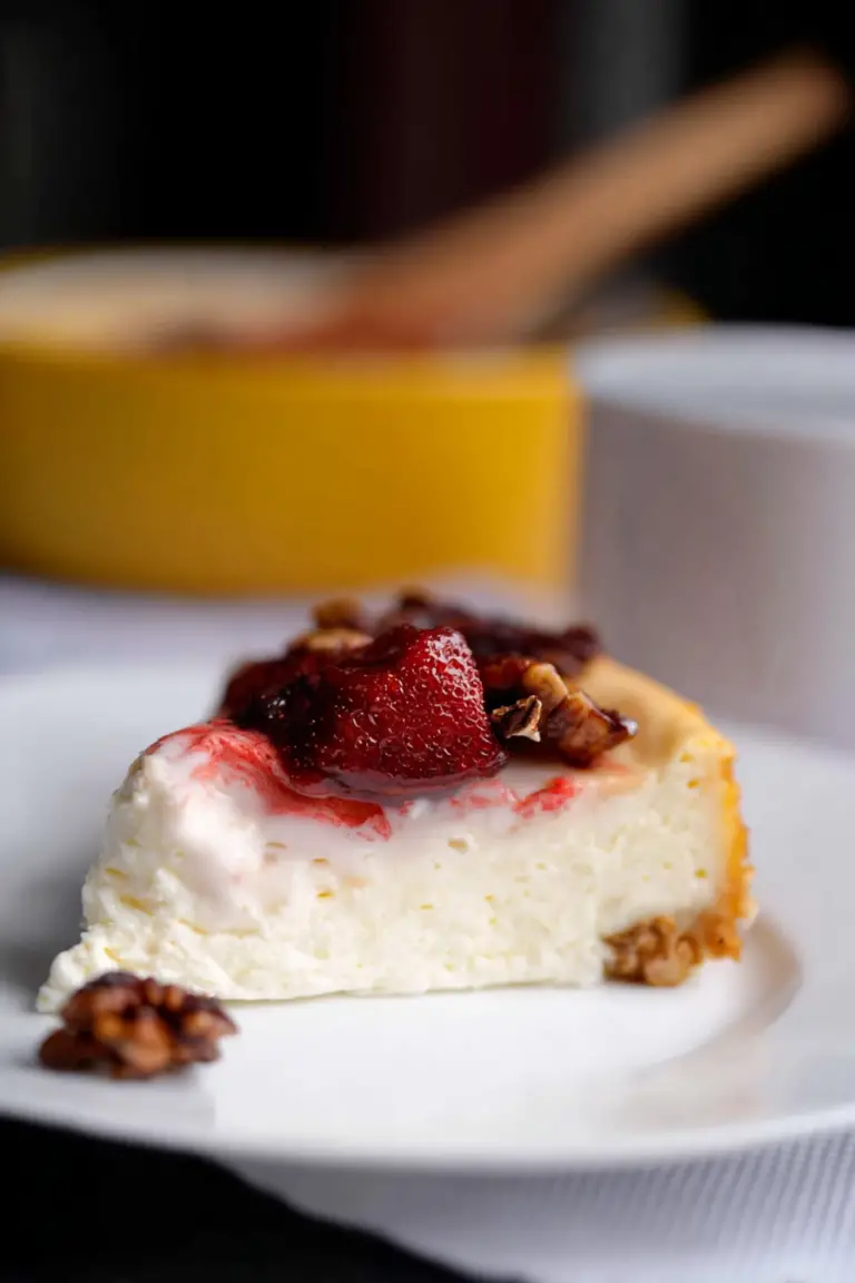 Slice of cottage cheese cheesecake topped with strawberries and granola on a wooden table.