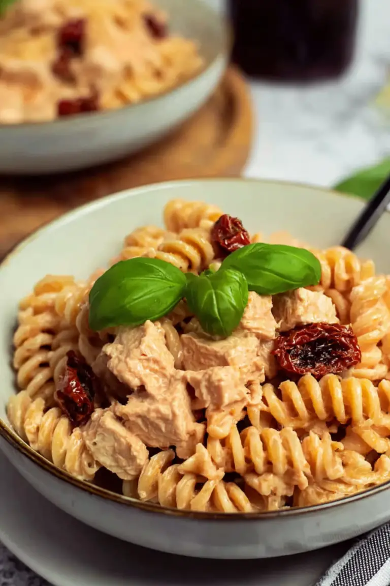 Creamy tofu pasta with sundried tomatoes, garnished with basil and olives on a wooden table.