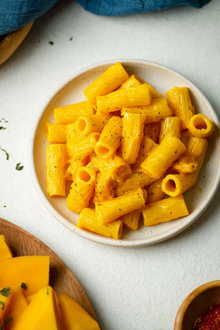 Creamy vegan butternut squash pasta with fresh herbs and nutritional yeast on a rustic table.