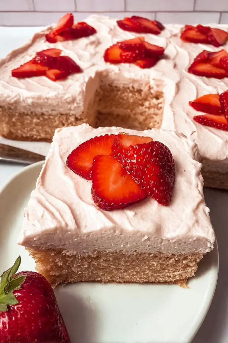 Fresh strawberry sheet cake with strawberry buttercream and fresh strawberries, sliced on a wooden table.