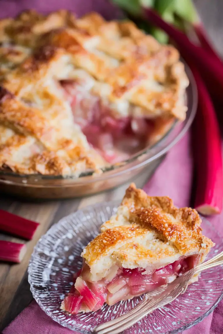 Freshly baked rhubarb pie with golden crust and red filling on a wooden table, served with vanilla ice cream.