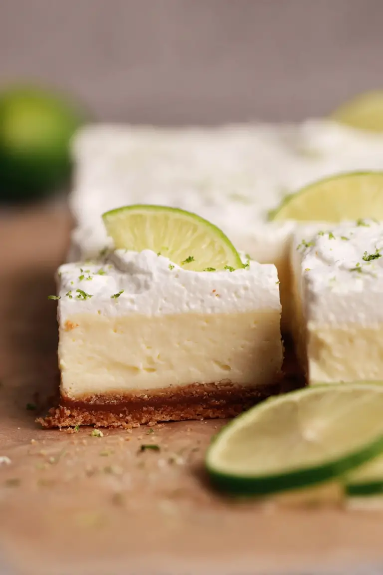 Delicious key lime pie bars topped with whipped cream and lime zest on a white plate.