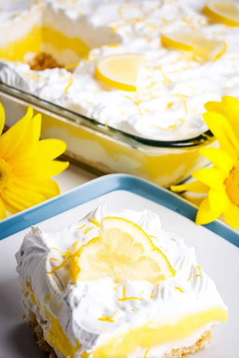 Slice of lemon lush dessert on a plate with lemon slices and zest, highlighting the layers of cream cheese and lemon pudding.