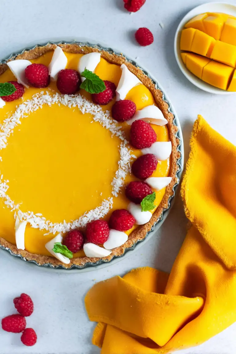 Mango curd tart with fresh mango slices and raspberries on a wooden table