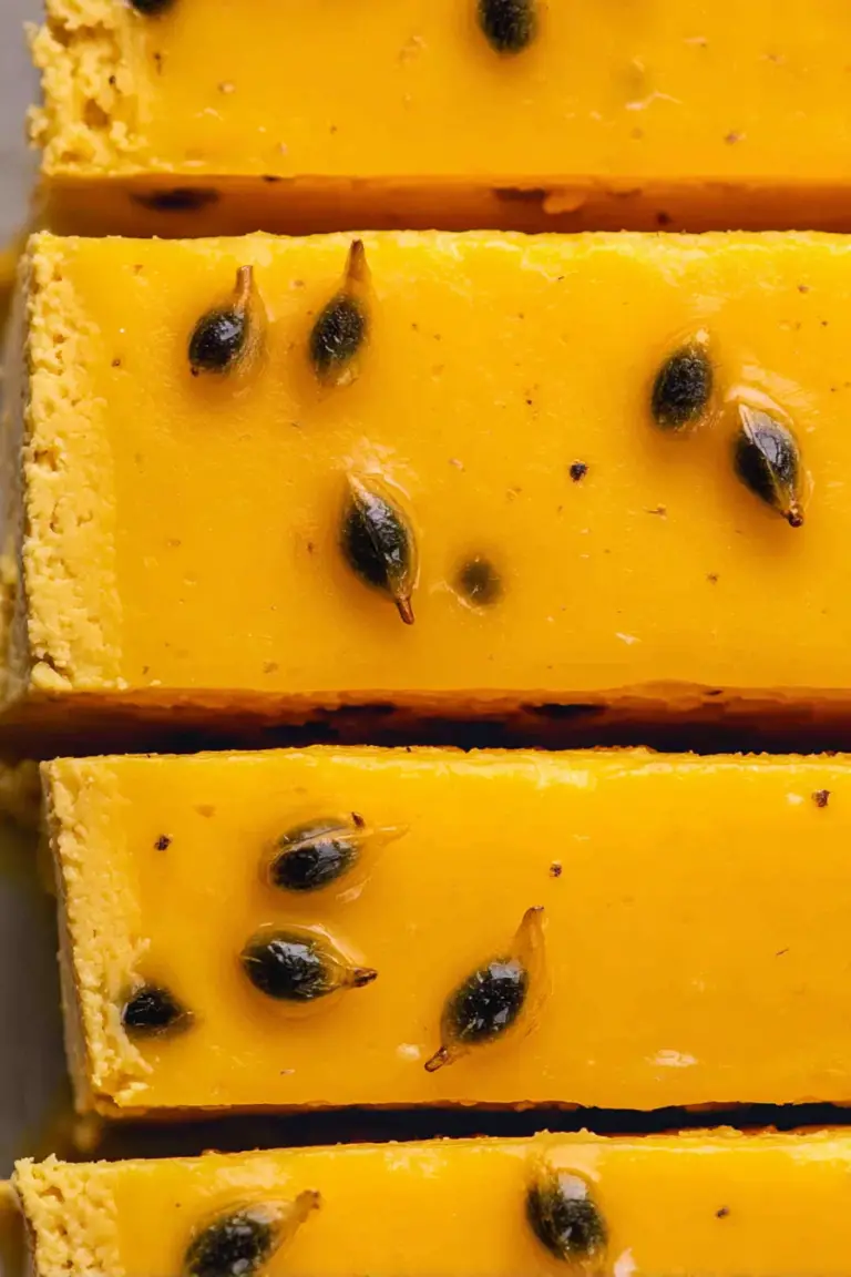 A slice of no bake passion fruit cheesecake with garnishes of fresh passion fruit and mint leaves on a white plate.