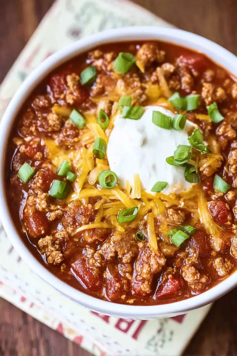 A delicious bowl of no bean chili topped with sour cream and diced onions, showcasing its rich color and texture.