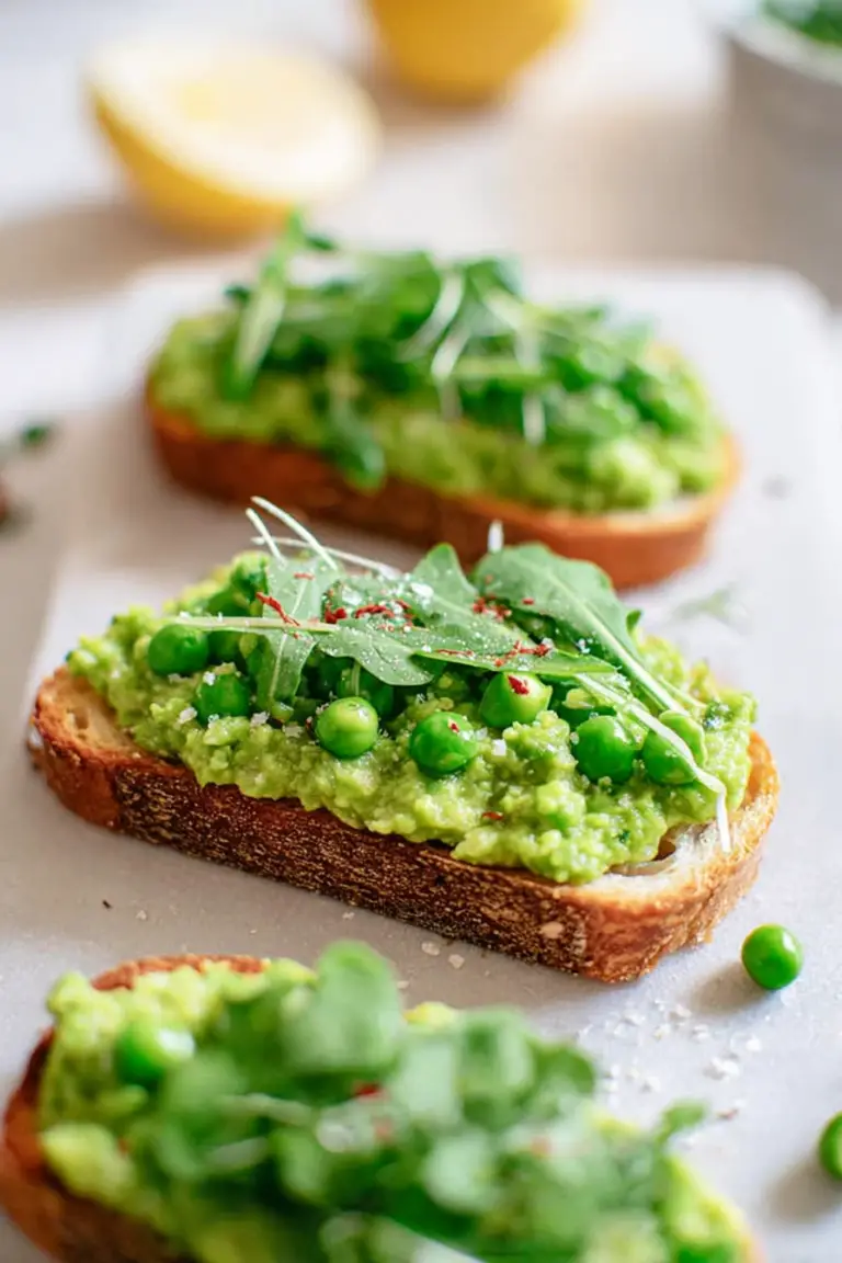 Plate of pea bruschetta with pea shoots and lemon zest on a wooden table.