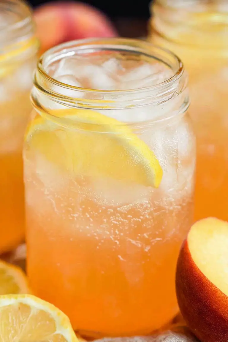 A glass of homemade peach lemonade decorated with lemon and peach slices on a rustic table.