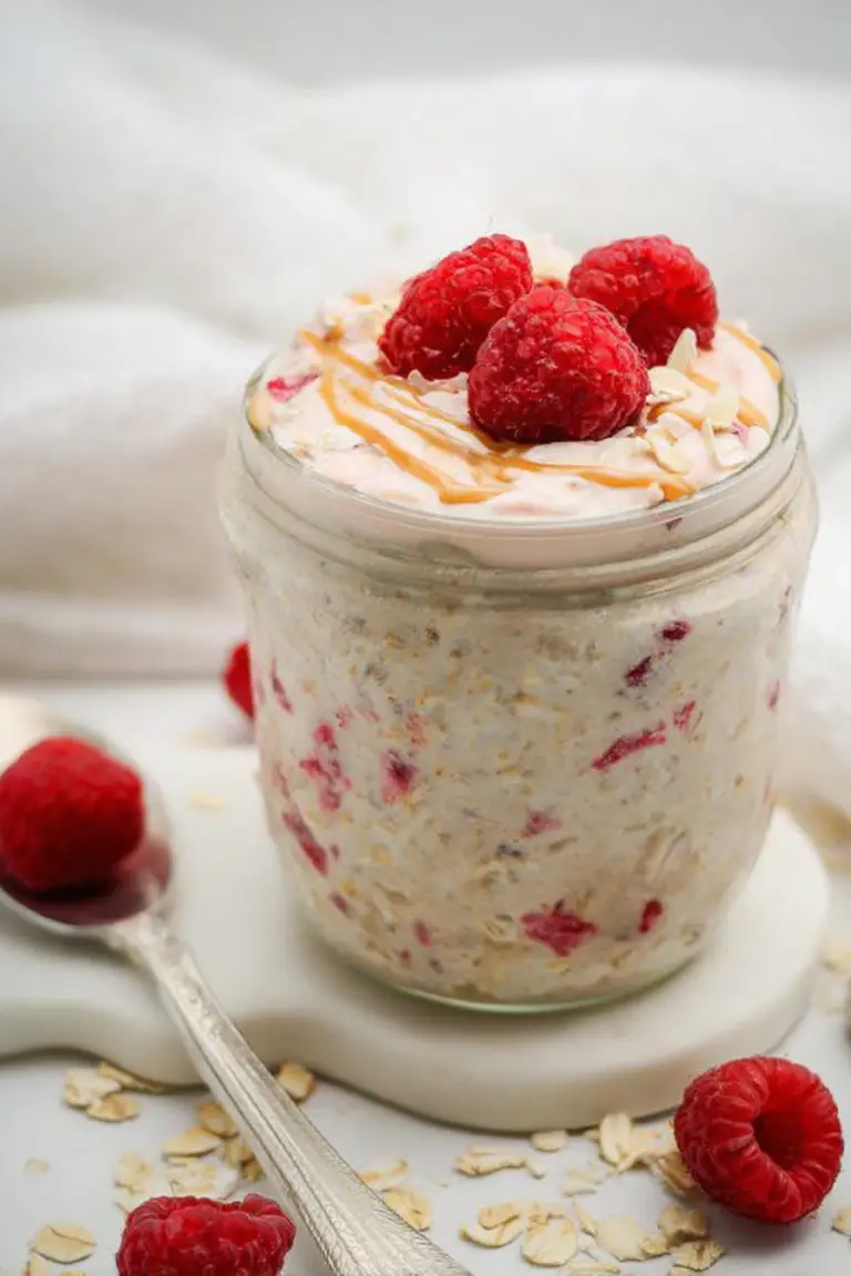 Close-up of raspberry cheesecake overnight oats in a jar, garnished with fresh raspberries and graham cracker crumbs.