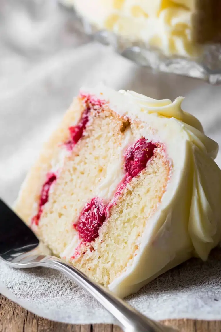 Slice of raspberry lemon cake on a wooden table with raspberries and lemon slices, showcasing the cake's moist texture and bright colors.