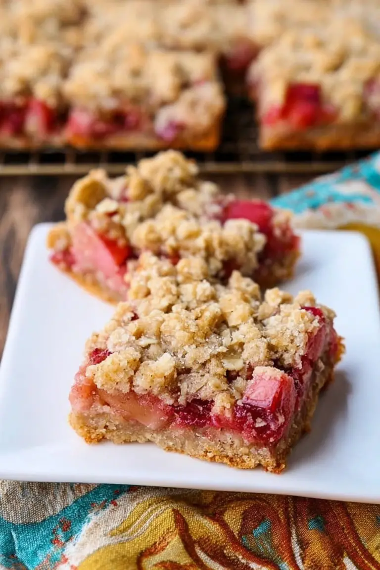 Close-up of rhubarb oatmeal bars garnished with fresh rhubarb slices and oats on a rustic wooden table.