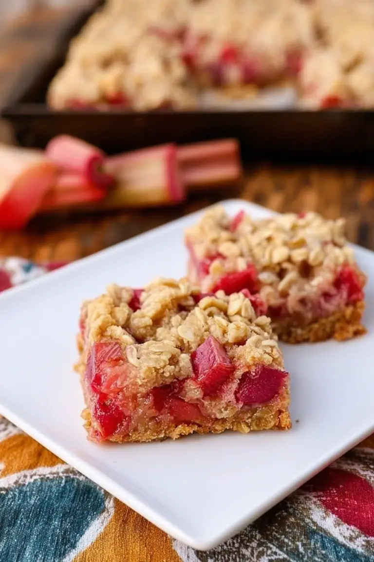Baked rhubarb oatmeal bars cut into squares on a wooden cutting board with rhubarb stalks.