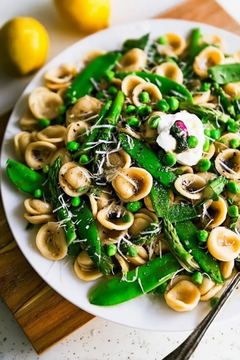 Bowl of Spring Orecchiette Pasta with Burrata, asparagus, and peas garnished with fresh herbs.