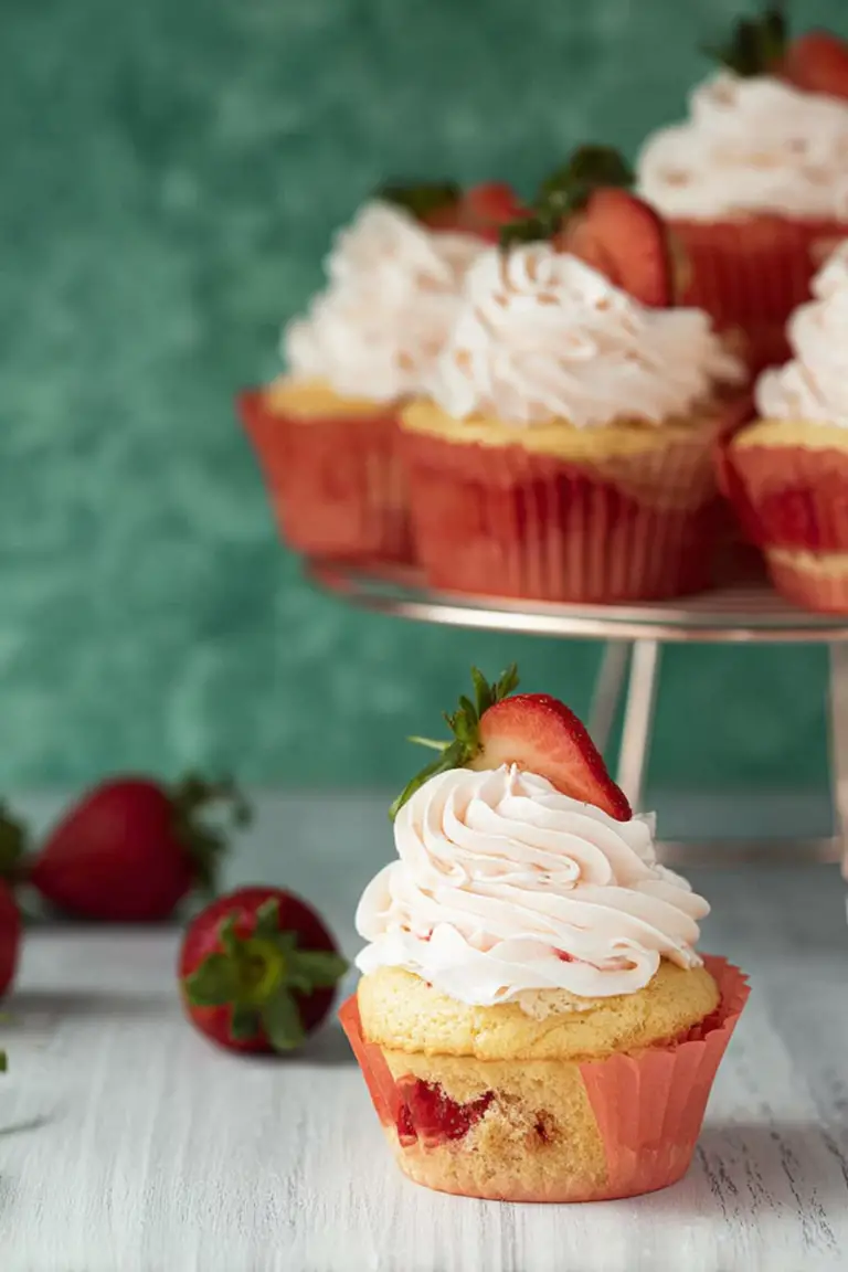 Close-up of a delicious strawberry filled cupcake topped with whipped cream and surrounded by fresh strawberries