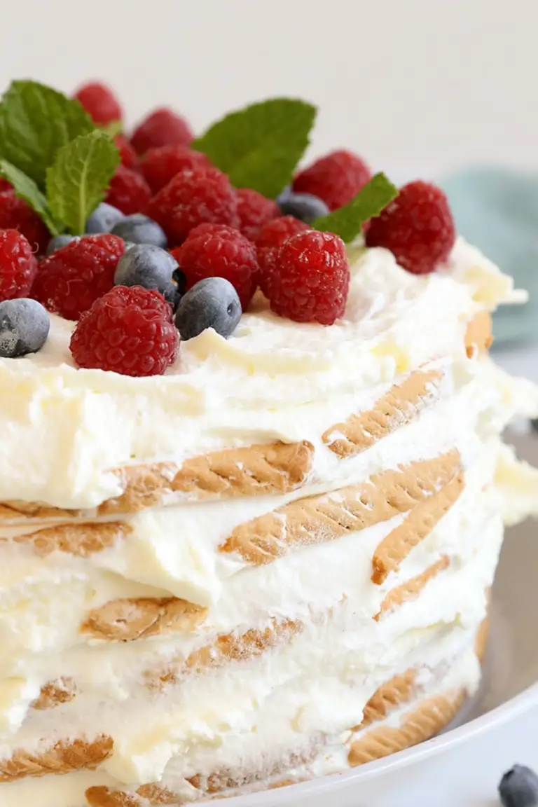 Slice of vanilla wafer icebox cake with fresh strawberries, blueberries, and mint on a white plate.