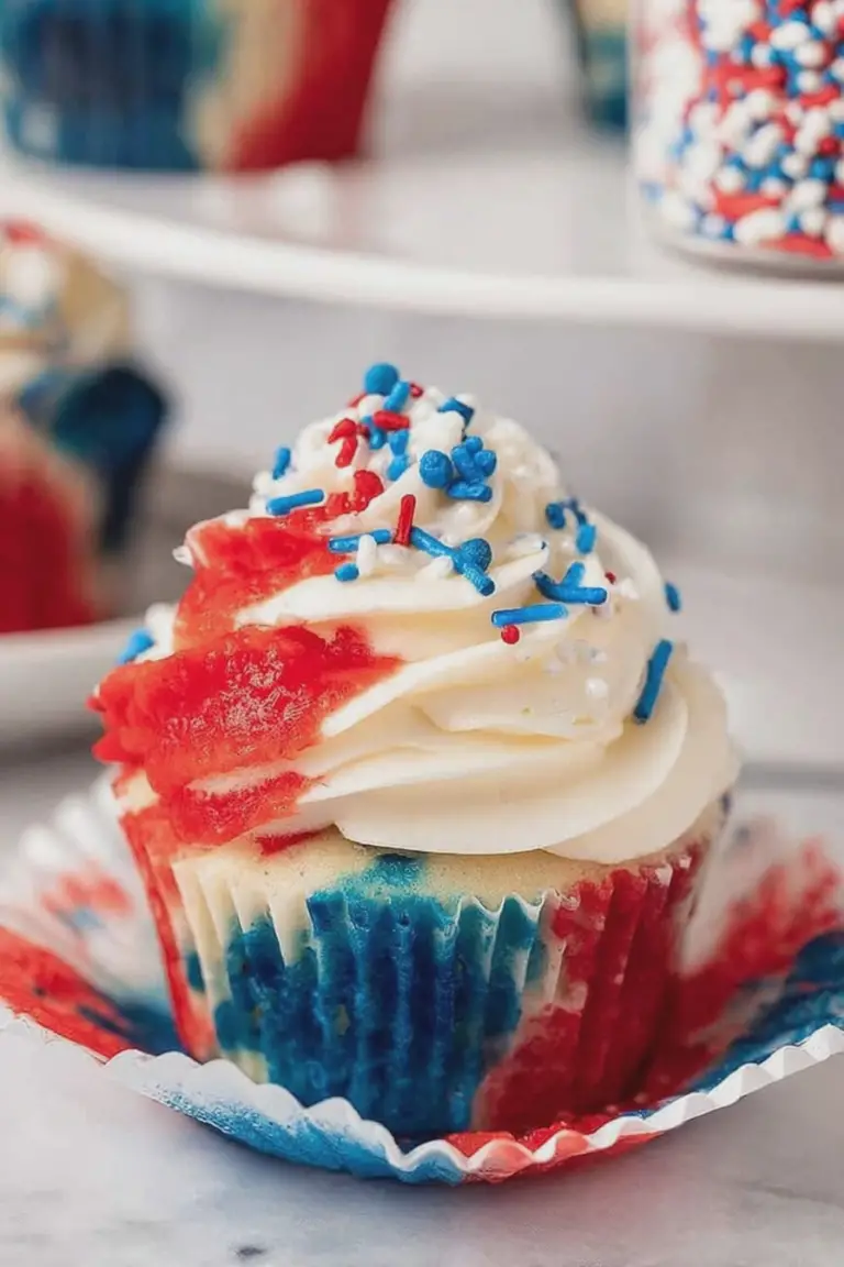 Festive 4th of July cupcake with red, white, and blue swirl frosting and sprinkles on a patriotic table.