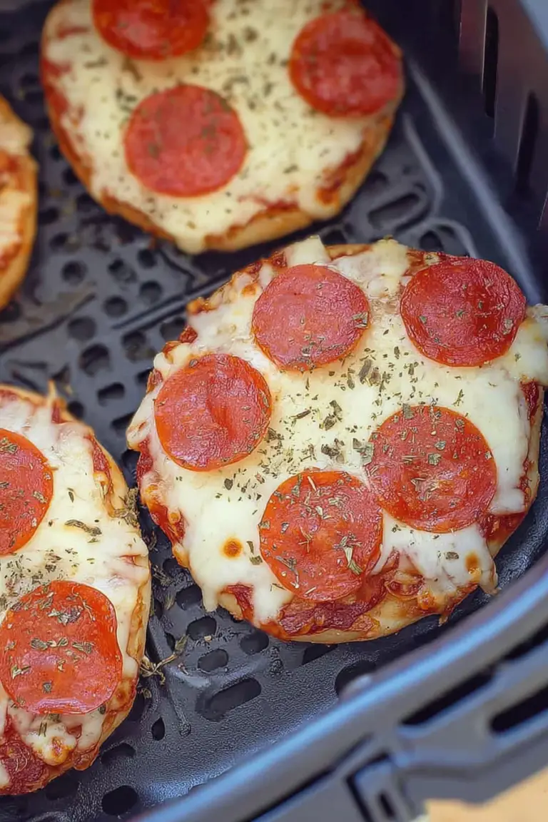 Delicious air fryer bagel pizza with melted cheese and fresh basil on a wooden board with marinara sauce.