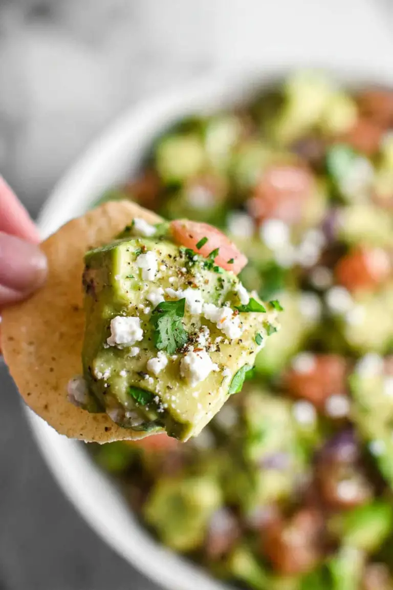 Delicious avocado feta dip in a bowl with parsley garnish, served with crackers and fresh tomatoes.