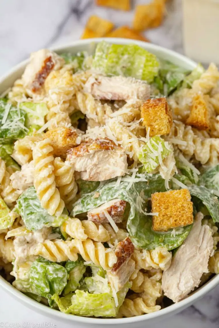 A colorful bowl of Chicken Caesar Pasta Salad with romaine, rotini, grilled chicken, croutons, and Parmesan cheese.