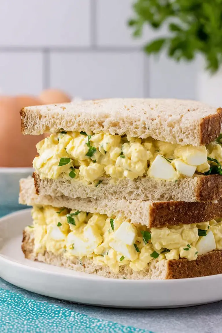Classic egg salad served with fresh herbs on a wooden table with slices of bread and a salad.