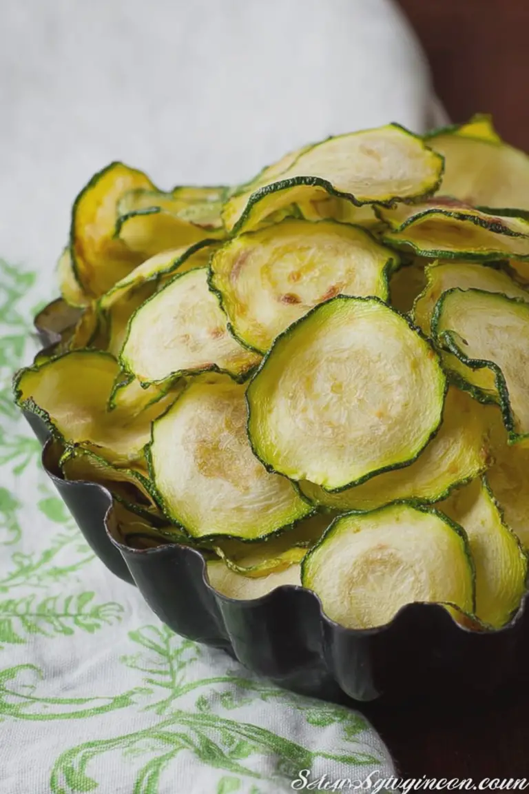 Crispy salt and vinegar zucchini chips in a bowl with fresh herbs and vinegar on the side.