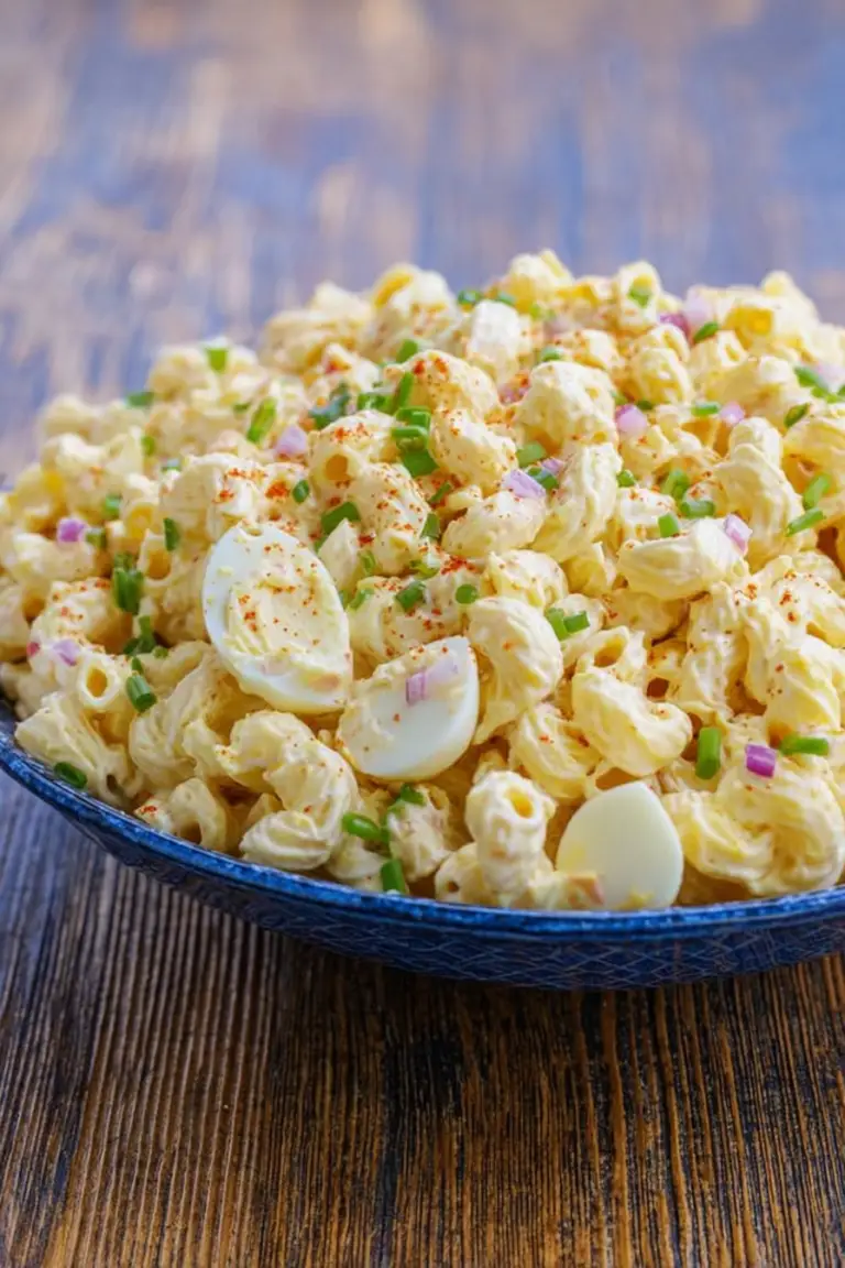 Deviled egg pasta salad in a bowl, topped with green onions and paprika, highlighting its creamy texture and vibrant colors.
