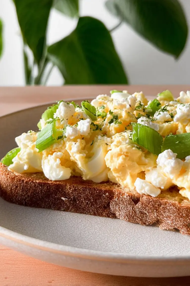 Egg salad with cottage cheese on toasted sourdough bread topped with avocado slices and fresh herbs.