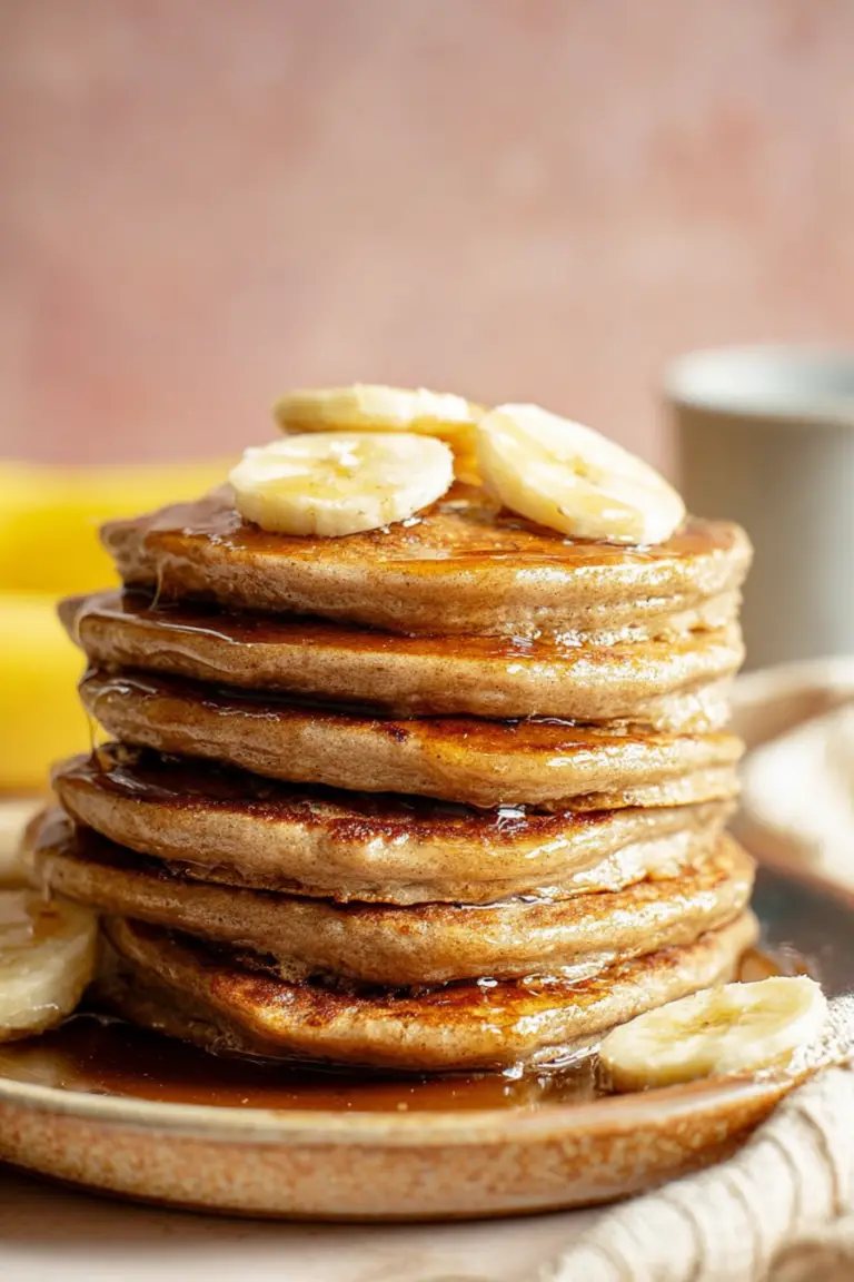 Fluffy healthy banana oatmeal pancakes stacked on a plate, topped with sliced bananas and drizzled with maple syrup.