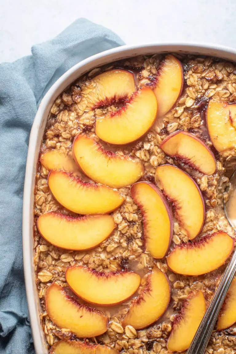 Bowl of fresh peach baked oatmeal topped with slices of peach and pecans, ideal for a healthy breakfast.