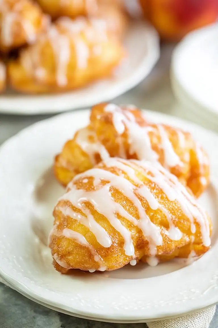 Delicious fresh peach fritters dusted with powdered sugar on a rustic wooden plate with fresh peaches.