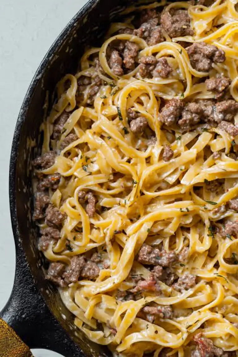 A delicious bowl of garlic butter beef pasta topped with parsley and parmesan on a wooden table.