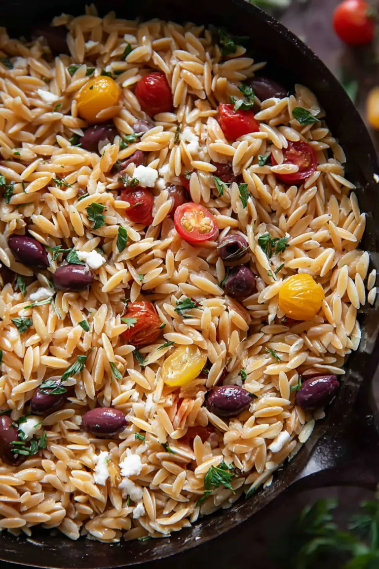 Greek Orzo with cherry tomatoes, feta cheese, and fresh basil in a bowl on a wooden table.